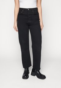 Svarta högmidjade jeans med rak passform, tillverkade av denim, med kopparfärgad hardvara och synliga framfickor. Kombinerat med svarta anklarstövlar.