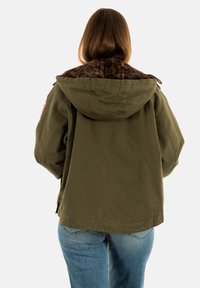 Persona con capelli castani lisci che indossa una giacca con cappuccio verde oliva con fodera in stampa leopardata e jeans blu, vista di spalle.