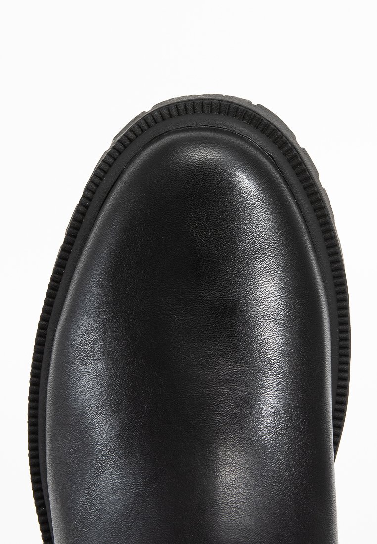 Stivale alla caviglia in pelle nera con punta arrotondata, suola in gomma e cuciture testurizzate lungo il bordo superiore. Finitura liscia.