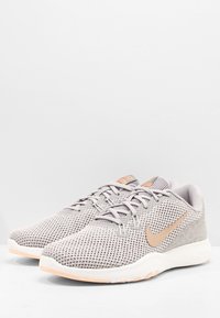 Szare siateczkowe trampki z teksturowanym wzorem, z jasnopomarańczowym logo i białą podeszwą środkową. Sznurowane za pomocą standardowego systemu oczek.