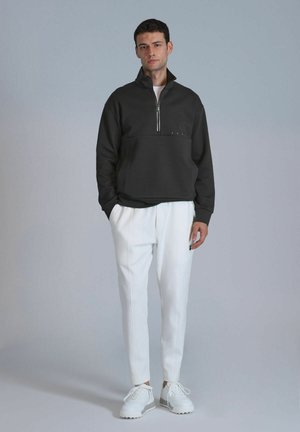 Donkergrijze ritspullover met een halve kraag, gedragen met witte op maat gemaakte broek en witte sneakers, met subtiele schouderdetails.