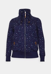 Sudadera con cremallera navy y cuello alto, con cordones y toggle de madera. Presenta un patrón de pájaros en azul claro y blanco sobre una tela suave.