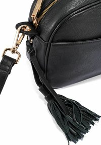 Czarna skórzana torebka o zaokrąglonym kształcie, ze złotymi akcentami, zamknięciem na zamek błyskawiczny i zielonym frędzlem. Teksturowana powierzchnia.