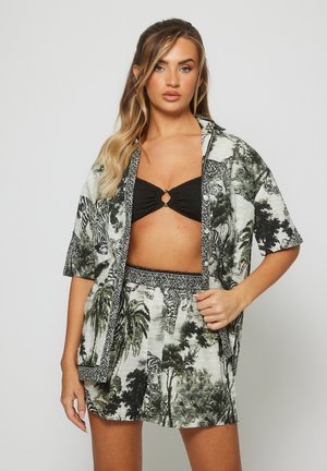 Tweedelig damesoutfit bestaande uit een shirt met korte mouwen en een rok. Gemaakt van lichtgewicht stof met een monochrome jungleprint en zwarte accenten.