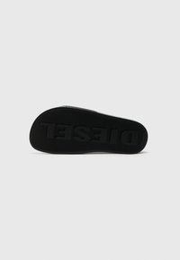 Semelle de chaussure en caoutchouc noir avec une surface texturée et le mot "DIESEL" en relief, présentant un talon arrondi et un design plat.