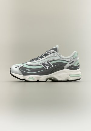 Pelēkas un baltas New Balance 1000 sporta kurpes ar gaiši zaļiem akcentiem, auklu aizdare un mīkstināta zolīte attēlots no sāniem.