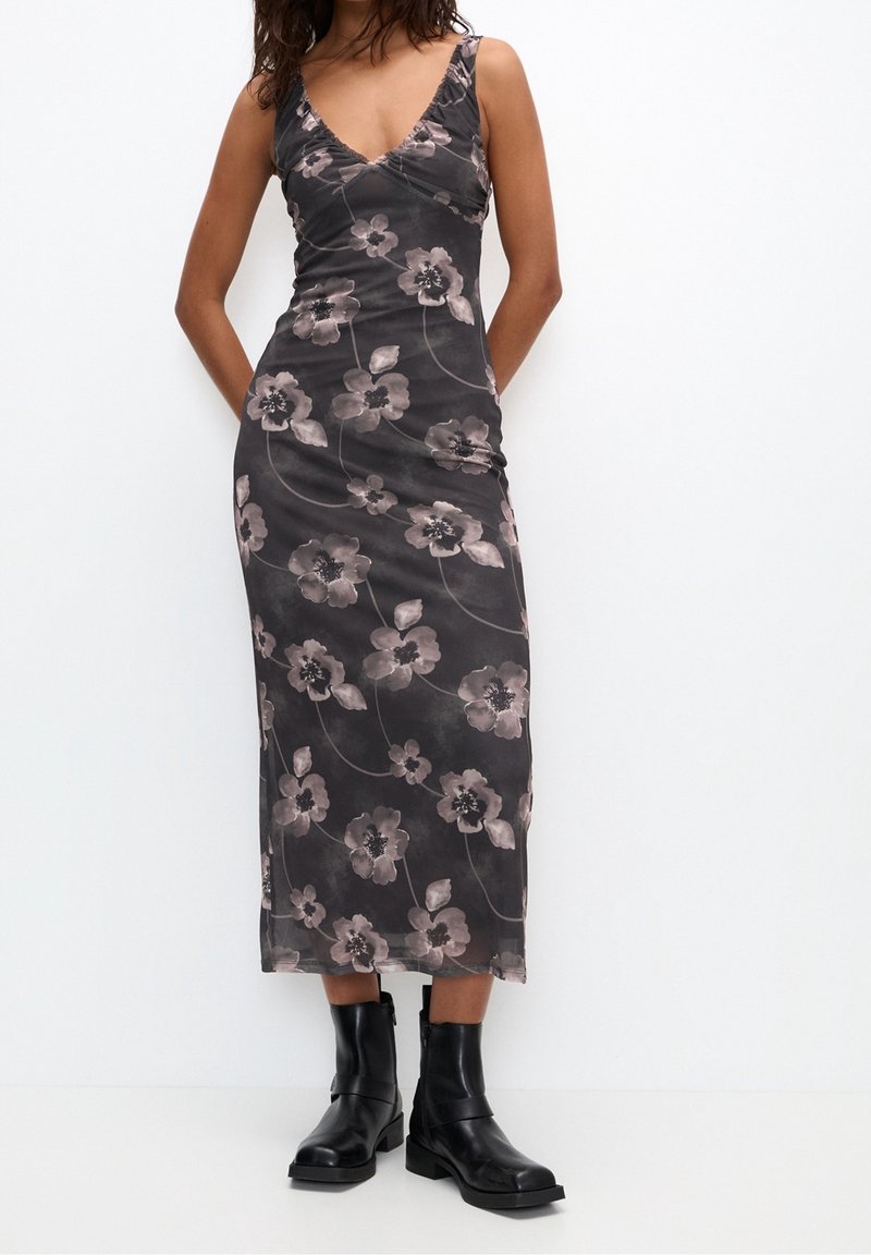 Robe sans manches à fleurs sombres avec un décolleté en V, fabriquée en tissu doux et transparent et près du corps, associée à des bottines noires à cheville.