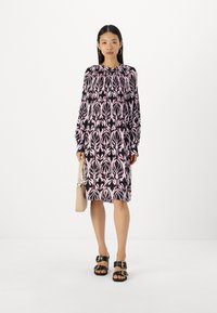 Schwarz und rosa gemustertes Kleid mit langen Ärmeln, Rundhalsausschnitt und lockerer Passform, kombiniert mit schwarzen Sandalen und einer beigefarbenen Handtasche.