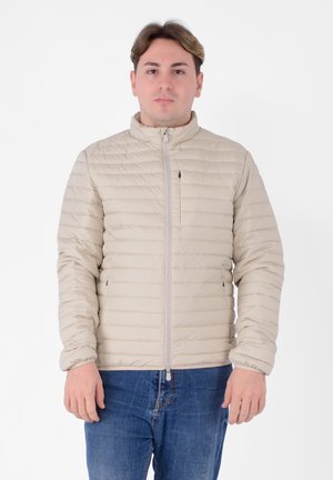 Giacca imbottita beige con motivo a righe orizzontali, chiusura con zip, collo alto e polsini elasticizzati. Indossata sopra jeans blu.