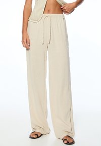 Beige wijde broek gemaakt van lichtgewicht stof met een trekkoord in de taille, voorzien van een zachte textuur en minimale stikseldetails.
