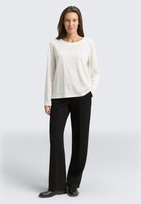 Haut blanc à manches longues avec de fines rayures, associé à un pantalon noir à jambes larges et des bottes noires. Design simple et moderne axé sur le confort.