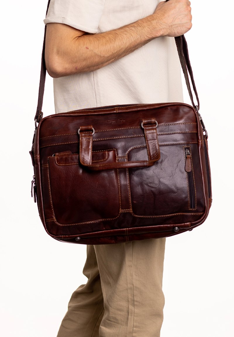 Borsa a tracolla in pelle marrone con due manici superiori e una lunga tracolla. Presenta diverse tasche e dettagli di cucitura. Texture liscia.