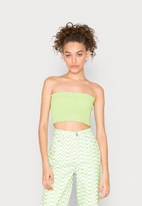 Top bandeau verde corto com textura franzida; combinado com calças de cintura alta com um padrão ondulado em branco e verde.