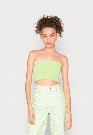 Top bandeau verde corto com textura franzida; combinado com calças de cintura alta com um padrão ondulado em branco e verde.