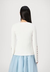 White ribbed long-sleeve top featuring cut-out accents on sleeves, paired with a light blue skirt for contrast. Simple design and texture.