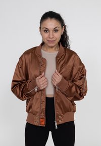Bronzen satijnen bomberjack met geribbelde kraag en manchetten, voorzien van ritsdetails en een logo op de voorkant. Glad textuur en een ontspannen pasvorm.