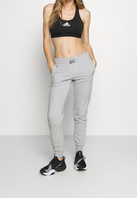 Svart atletisk sport-bh med vit logotyp, kombinerad med ljusgrå joggingbyxor med elastisk midja och sidofickor. Svarta sneakers.