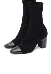 Botines negros con un upper de tela suave y punta afilada. Presentan una puntera de cuero y un tacón grueso.