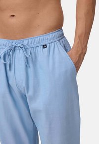 Lichtblauwe loungebroek gemaakt van zachte stof, met een elastische tailleband met een trekkoord en zijzakken. Klein logoaccent aanwezig.