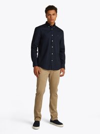 Navy-Button-Down-Hemd mit langen Ärmeln, khakifarbene Chinos und dunklen Sneakers. Merkmale: klassischer Kragen und Logoakzent auf dem Hemd.