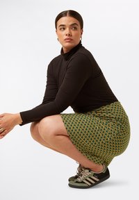Musta ribbed turtleneck, kuvioitu vihreä hame geometrisella designilla ja harmaa-mustan väriset lenkkarit. Asusteessa on istuva siluetti.