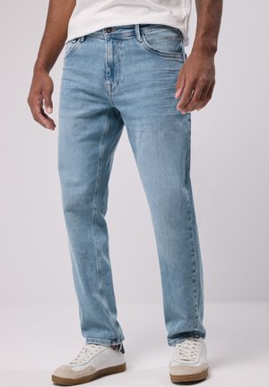 Light blue denim jeans with a straight-leg design, featuring five pockets and minimal fading, paired with white and gray sneakers.