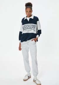 Felpa navy e grigia con stampa "MISSISSIPPI", design con colletto e vestibilità rilassata, abbinata a pantaloni della tuta grigi chiari e sneakers bianche.