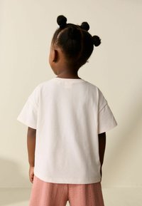 Tricou alb cu mâneci scurte și guler rotund, cu o croială lejeră. Tricoul este asortat cu pantaloni scurți roz texturați.