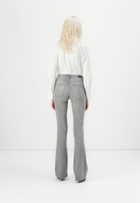 Grå vide jeans med en tett midje, to baklommer og lett slitasje. Båret med en hvit langermet skjorte, sett fra baksiden.