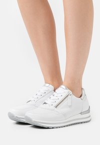 Vita lädersneakers med silverdetaljer, rund tå, perforerade detaljer och dragkedja på sidan. Tjock, vadderad sula.