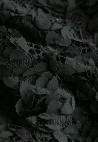 Zwarte stof met een bloemenkantstructuur, voorzien van gelaagde, cirkelvormige appliqués. Het oppervlak heeft een mix van gladde en gestructureerde secties.