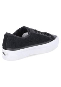 Baskets noires avec un dessus en tissu texturé, des accents en caoutchouc noir solide et une semelle plateforme blanche avec des côtes subtiles.