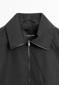 Giacca nera con cerniera argentata, colletto ampio e etichetta Massimo Dutti all'interno del collo.