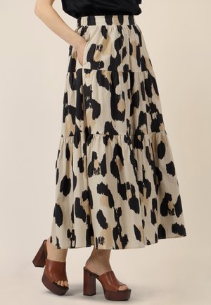 Woman wearing a tiered, calf-length skirt with black and beige abstract spots, brown high-heeled slide sandals, and a black top.