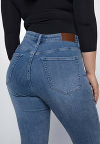 Blaue Jeans aus Denim mit glatter Textur, hoher Taille und Gesäßtaschen. Verfügt über ein braunes Leder-Logopatch am Bund.