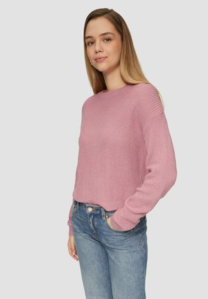 Jasnoróżowy sweter z dzianiny z prążkowanymi detalami i okrągłym dekoltem, zestawiony z niebieskimi dżinsami. Miękka tekstura, luźny krój.