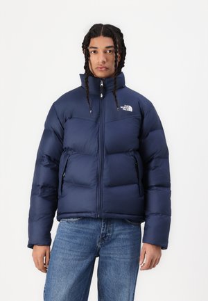 Giacca puffer navy con colletto alto, design trapuntato, zip frontale e tasche laterali; presenta un logo sul lato sinistro del petto.