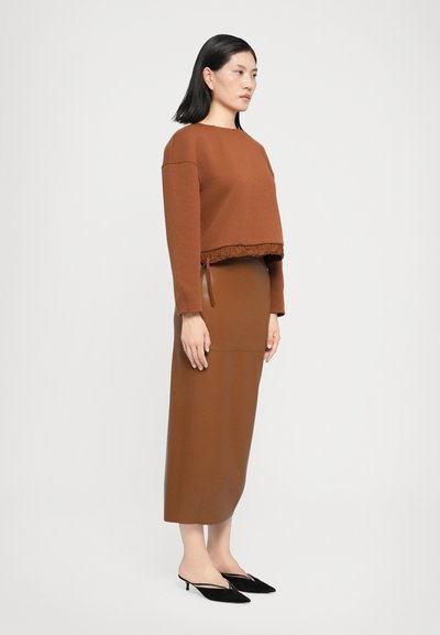 Hnědý zkrácený svetr s volánovým lemem, doplněný o hnědou přiléhavou sukni. Černé lodičky na podpatku outfit dotvářejí. Jednoduchá barva, hladká textura.