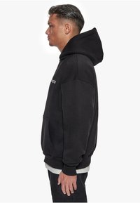 Schwarzer Hoodie mit großer Kapuze, Fronttasche und gerippten Bündchen. Aus weichem Stoff, verfügt über ein minimalistisches Design und eine gestickte Logo-Applikation.