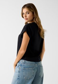 Czarny, krótki t-shirt z podwiniętymi rękawami, połączony z jasnoniebieskimi, postrzępionymi jeansami. Prosty, codzienny design; gładka tekstura.