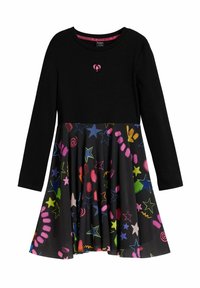 Schwarzes langärmeliges Kleid mit einem bunten, gemusterten Rock, der Sterne, Wirbel und Formen in Pink, Grün und Blau auf schwarzem Hintergrund zeigt.