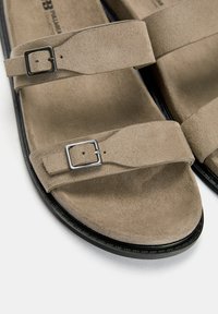 Brown suede sandals with two adjustable straps featuring silver-tone buckles. Soft texture and a contoured footbed, black sole.