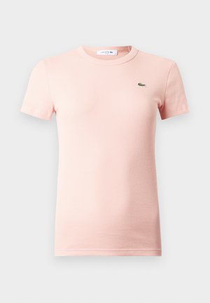 T-shirt rosa claro com mangas curtas caneladas, gola redonda e um pequeno logótipo verde do crocodilo Lacoste no lado esquerdo do peito.