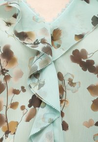 Tissu bleu clair avec impression florale marron et beige, avec un bord doux froncé et une texture délicate et transparente.