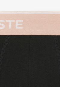 Zwarte katoenen stof met verticale stikdetails en een beige elastische tailleband met gedeeltelijke witte letters "STE".