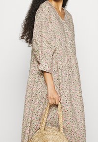 Vestido de longitud a la rodilla con estampado floral en color beige claro con flores rosas y verdes, que presenta un escote en V, hombros fruncidos y un ajuste relajado.
