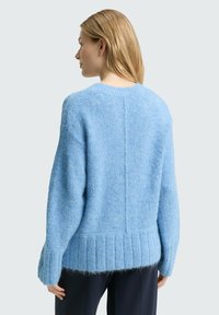 Jasnoniebieski sweter z dzianiny o luźnym kroju, z prążkowanym dołem i miękką fakturą. Posiada zaokrąglony dekolt i długie rękawy.