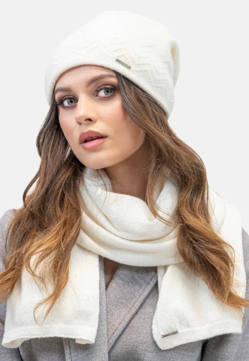 Bonnet tricoté blanc avec un motif texturé et une accent argentée, accompagné d'une écharpe blanche assortie en un matériau doux et luxueux.