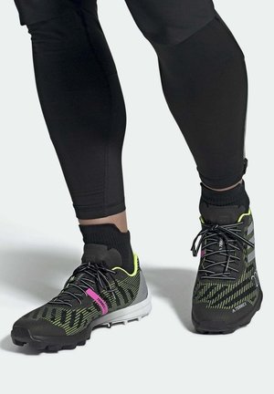 Černé sportovní boty se strukturovaným síťovaným svrškem, žlutými akcenty a růžovým brandingem. Gumová podešev s mnohostrannými záběrovými výstupky.