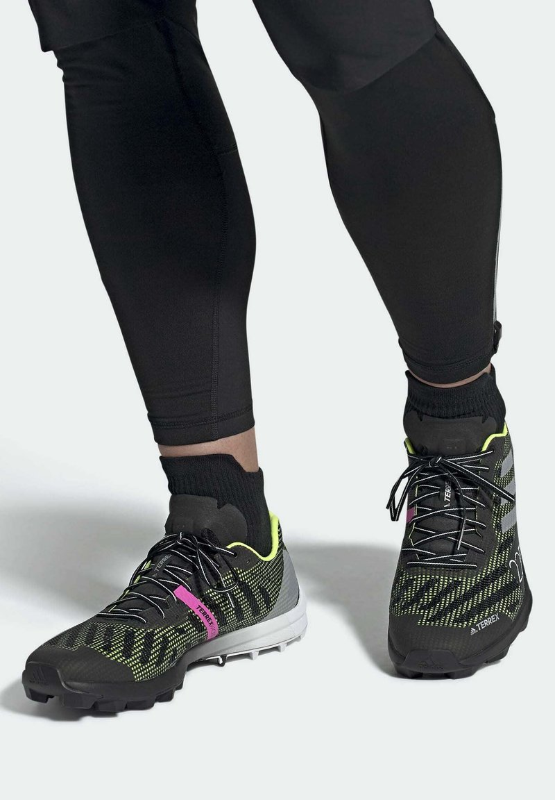 Czarne sportowe buty z teksturowana siateczką, żółtymi akcentami i różowym brandingiem. Gumowa podeszwa z wielokierunkowym bieżnikiem.